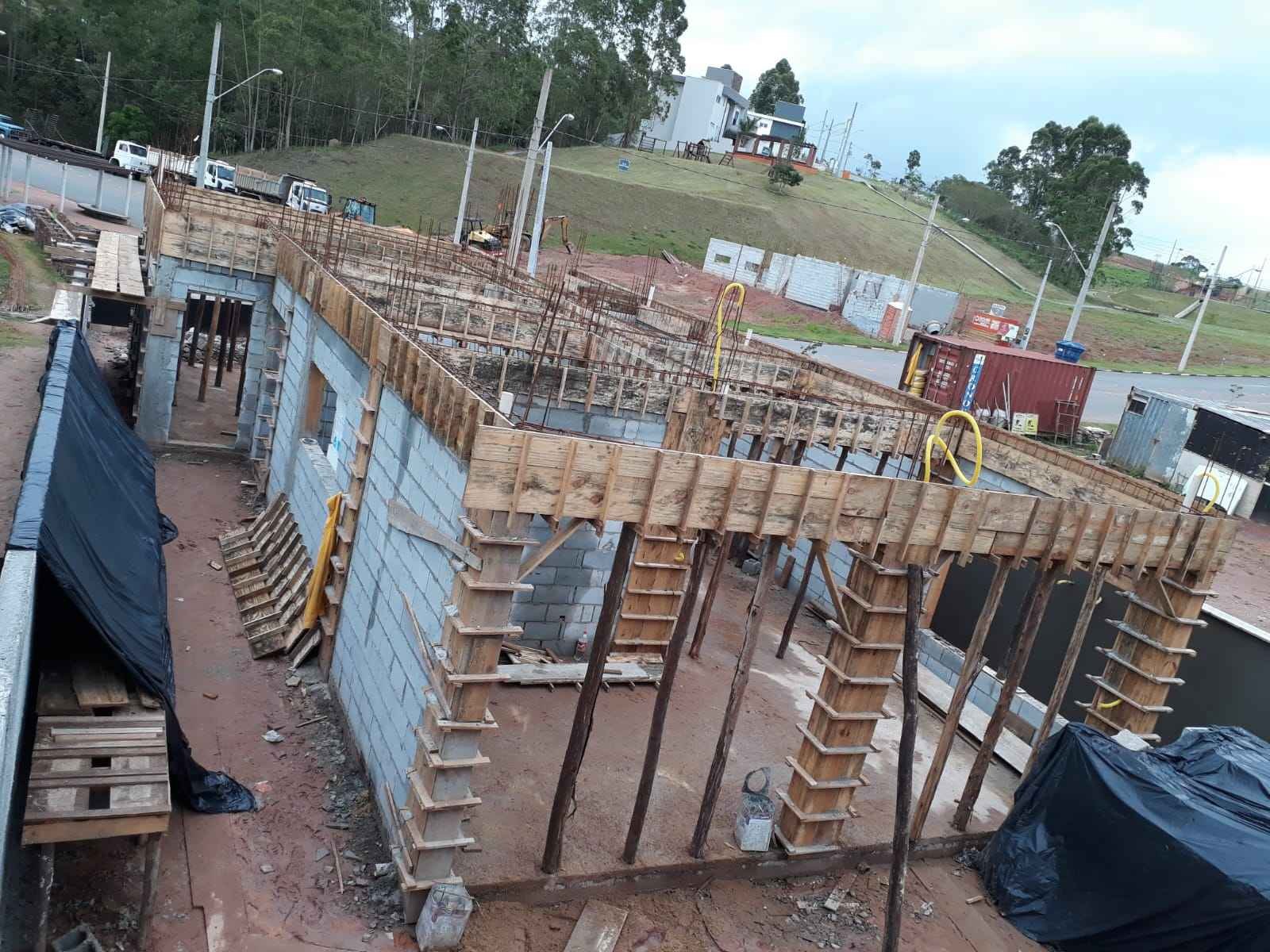 Obra residencial em fase estrutural com formas de madeira, escoramento e alvenaria em execução
