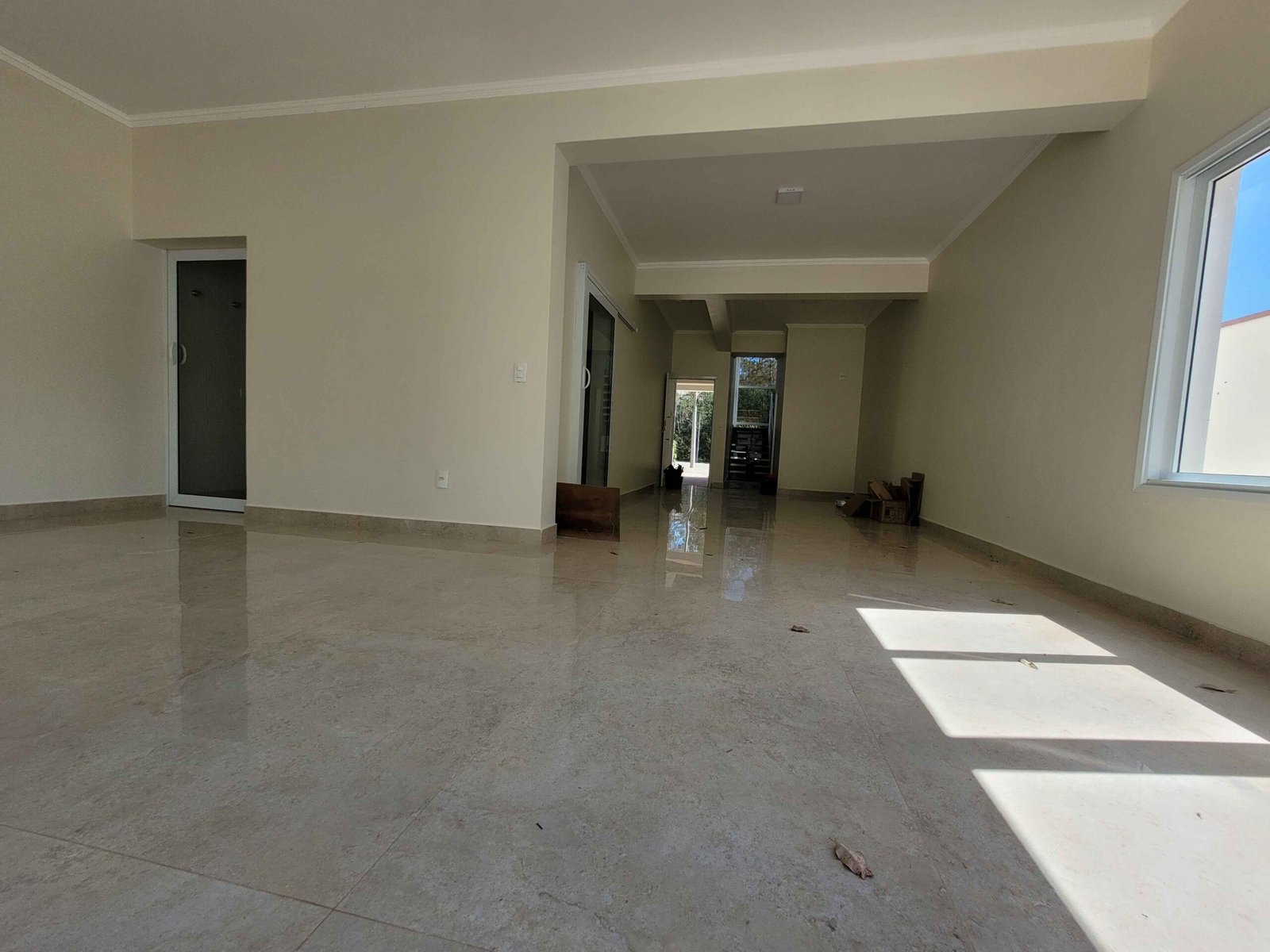 Sala ampla de residência de alto padrão com piso claro, paredes finalizadas e iluminação natural